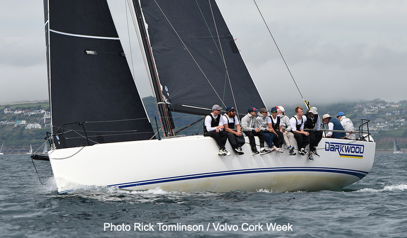 Sailors balancing on the edge of a racing yacht during a cloudy day.