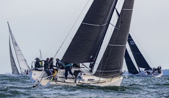 Sailors adjusting sails on a racing yacht in windy conditions.