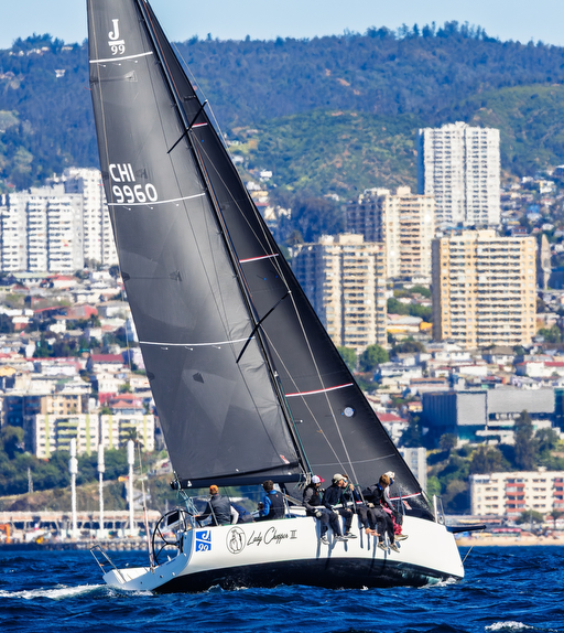 Sailboat with crew sailing near city skyline.